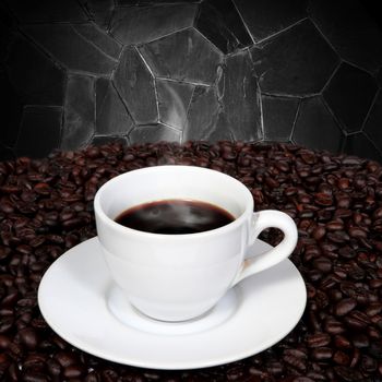 Black coffee in cup and coffee beans with smoke on granite wall background.