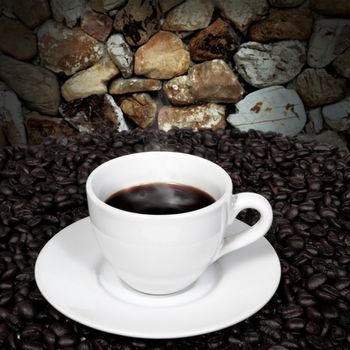 Black coffee in cup and coffee beans with smoke on stone wall background.