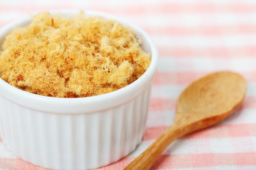 dried pork floss in white cup with wooden spoon on napery background.  
