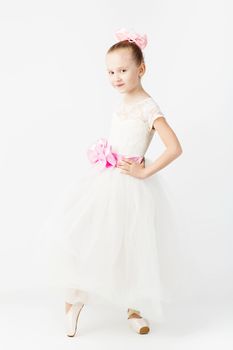 Beautiful ballet dancer on white background. Slender little ballerina girl in white dress and in pointe shoes