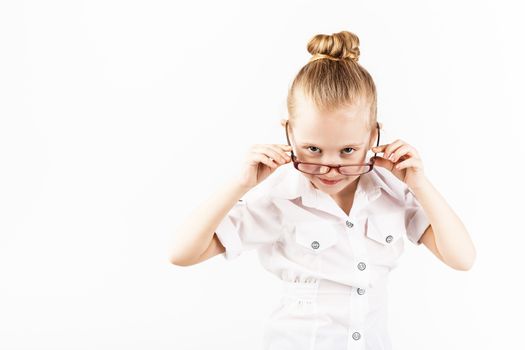 Funny little girl wearing eyeglasses imitates a strict teacher against white background. Little student Looking at camera. School concept. Back to School