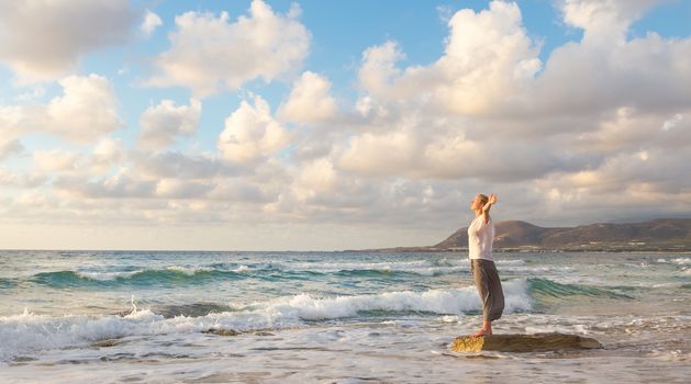 Relaxed woman enjoying sun, freedom and life an beautiful beach in sunset. Young lady feeling free, relaxed and happy. Concept of vacations, freedom, happiness, enjoyment and well being.