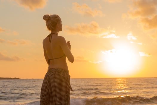 Silhouette of young woman practicing yoga on sandy beach at sunset.