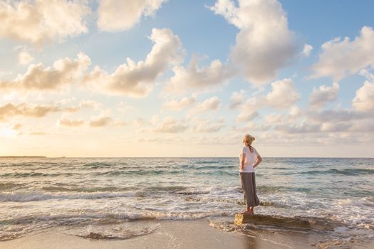 Relaxed woman enjoying sun, freedom and life an beautiful beach in sunset. Young lady feeling free, relaxed and happy. Concept of vacations, freedom, happiness, enjoyment and well being.