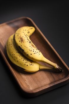 Two organic bananas in a wood sish over a black board.