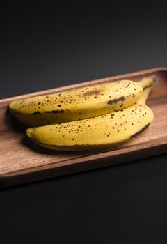 Two organic bananas in a wood sish over a black board.
