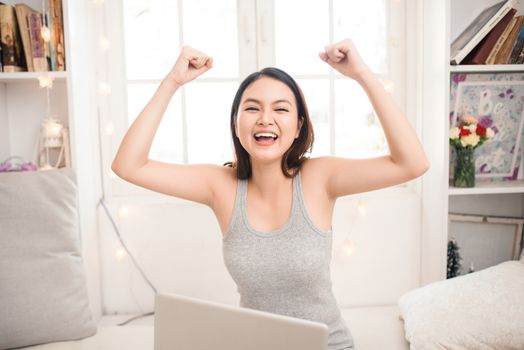 Happy excited asian young woman working on a laptop at home.