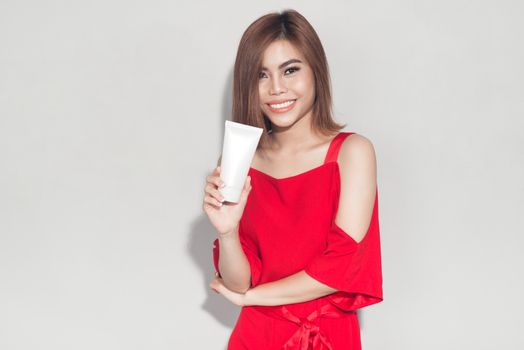 Portrait of cheerful smiling fashion girl in red dress holding cosmetic plastic tube