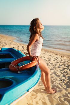 Beautiful young woman relaxing on the beach. She is standing next to boat and sunbathing.