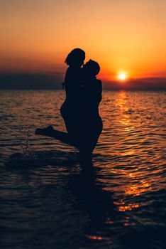 Silhouette of a loving couple hugging and kissing at sunset on the beach.