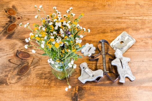 Tin Cookie Cutters and Flowers in Glass Vase Sitting on Wooden Table With Knots
