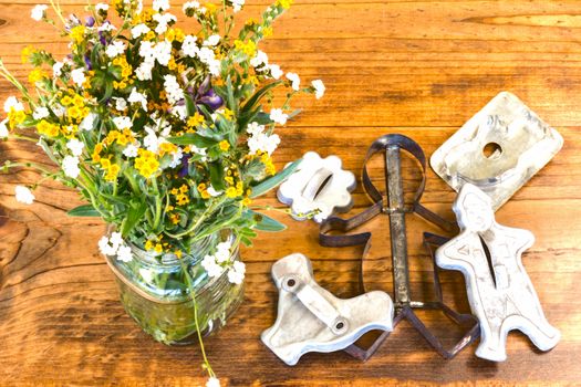 Tin Cookie Cutters and Flowers in Glass Vase Sitting on Wooden Table With Knots