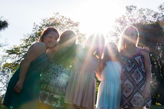 Young Girls Standing Together in Green Field With Trees in the Background and Sunlight Overhead