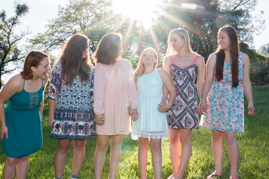 Young Girls Standing Together in Green Field With Trees in the Background and Sunlight Overhead