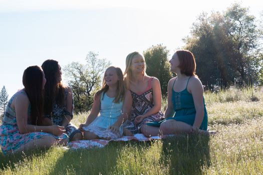 Group of Girls Sitting Together in Grassy Field With Sunlight Overhead