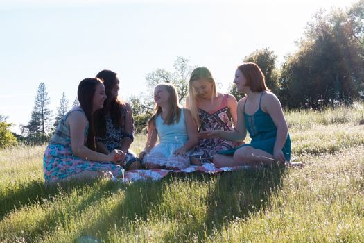 Group of Girls Sitting Together in Grassy Field With Sunlight Overhead