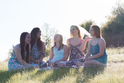 Group of Girls Sitting Together in Grassy Field With Sunlight Overhead