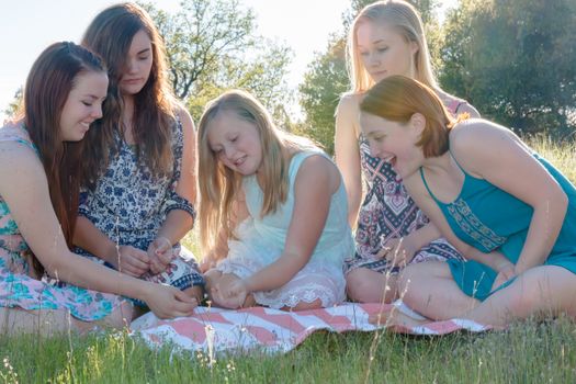 Group of Girls Sitting Together in Grassy Field With Sunlight Overhead