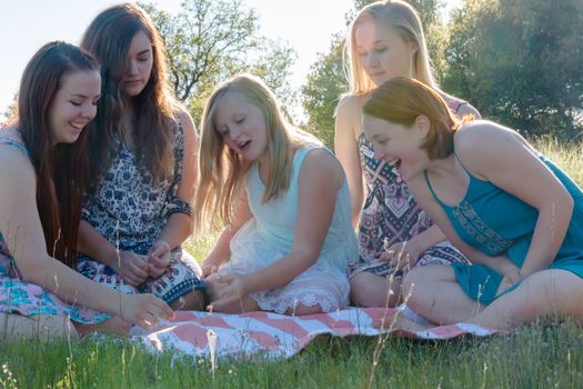 Group of Girls Sitting Together in Grassy Field With Sunlight Overhead