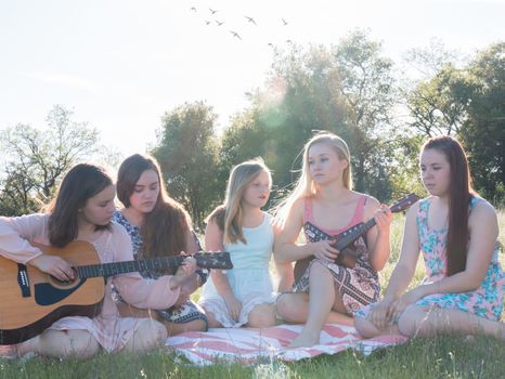 Young Girls Sitting Together in Grassy Field Singing and Playing Musical Instruments With Sunlight Overhead