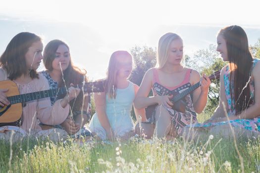 Young Girls Sitting Together in Grassy Field Singing and Playing Musical Instruments With Sunlight Overhead