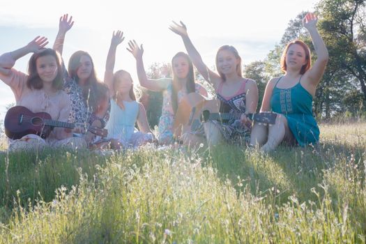 Young Girls Sitting Together in Green Grassy Field Singing and Playing Musical Instruments With Arms Raised up