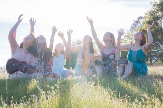 Young Girls Sitting Together in Green Grassy Field Singing and Playing Musical Instruments With Arms Raised up