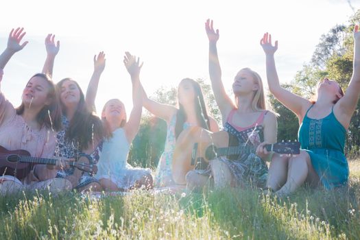 Young Girls Sitting Together in Green Grassy Field Singing and Playing Musical Instruments With Arms Raised up