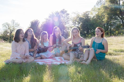 Young Girls Sitting Together in Grassy Field Singing and Playing Musical Instruments With Sunlight Overhead