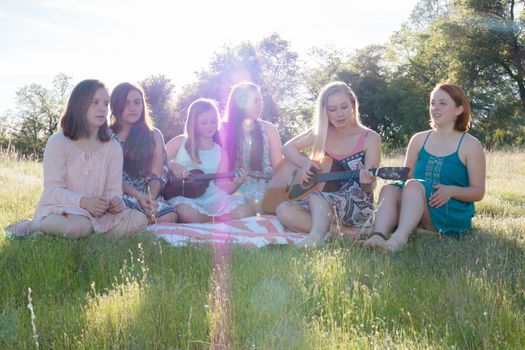 Young Girls Sitting Together in Grassy Field Singing and Playing Musical Instruments With Sunlight Overhead