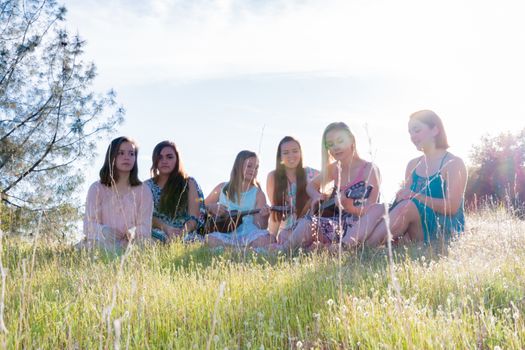 Young Girls Sitting Together in Grassy Field Singing and Playing Musical Instruments With Sunlight Overhead