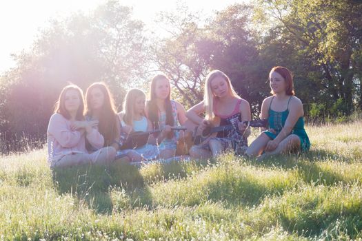 Young Girls Sitting Together in Grassy Field Singing and Playing Musical Instruments With Sunlight Overhead