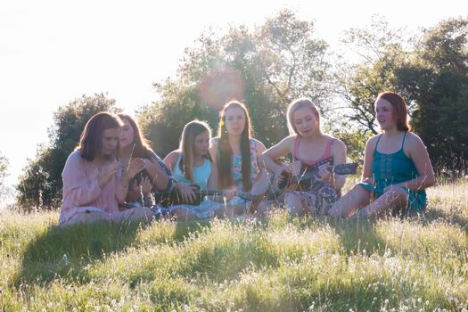 Young Girls Sitting Together in Grassy Field Singing and Playing Musical Instruments With Sunlight Overhead