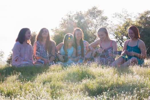 Young Girls Sitting Together in Grassy Field Singing and Playing Musical Instruments With Sunlight Overhead