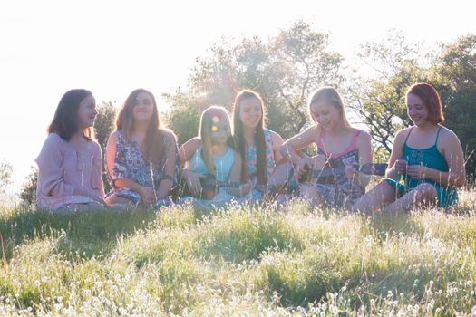 Young Girls Sitting Together in Grassy Field Singing and Playing Musical Instruments With Sunlight Overhead