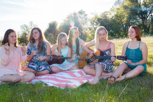 Young Girls Sitting Together in Grassy Field Singing and Playing Musical Instruments With Sunlight Overhead