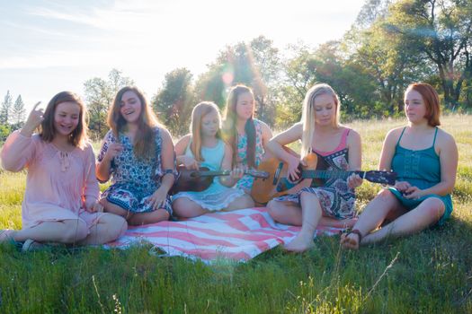 Young Girls Sitting Together in Grassy Field Singing and Playing Musical Instruments With Sunlight Overhead