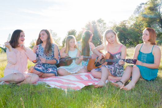 Young Girls Sitting Together in Grassy Field Singing and Playing Musical Instruments With Sunlight Overhead