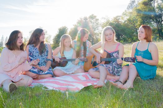 Young Girls Sitting Together in Grassy Field Singing and Playing Musical Instruments With Sunlight Overhead