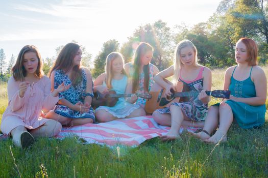 Young Girls Sitting Together in Grassy Field Singing and Playing Musical Instruments With Sunlight Overhead