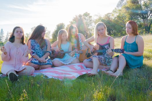 Young Girls Sitting Together in Grassy Field Singing and Playing Musical Instruments With Sunlight Overhead