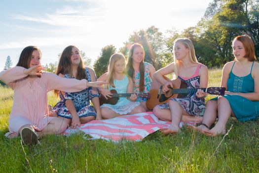 Young Girls Sitting Together in Grassy Field Singing and Playing Musical Instruments With Sunlight Overhead