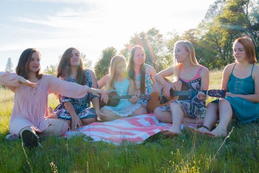 Young Girls Sitting Together in Grassy Field Singing and Playing Musical Instruments With Sunlight Overhead