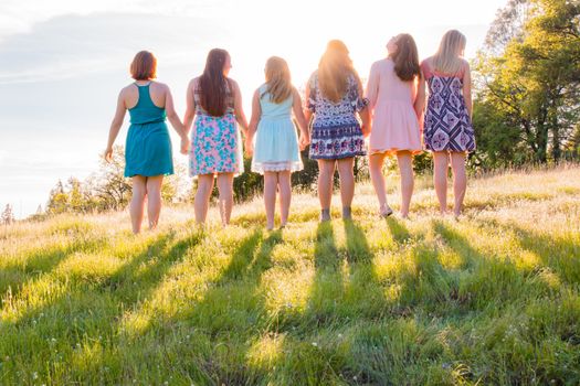Young Girls Standing Together in Grassy Field Facing the Bright Sunset