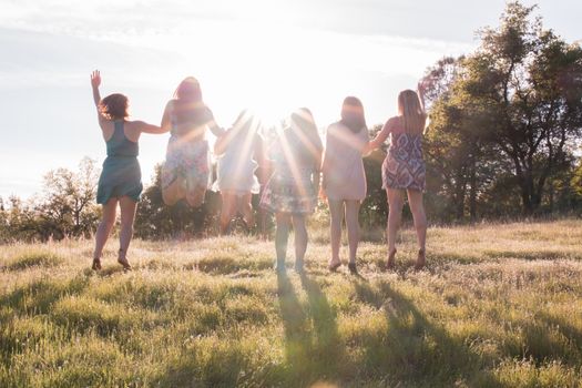 Girls Standing and Jumping Together Facing the Bright Sunset