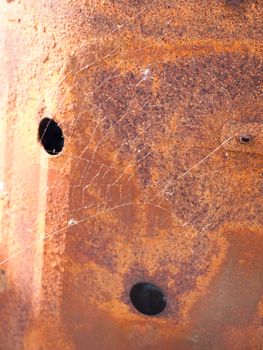 a thin spiderweb on the side of some rusted metal in light outside in the field in spring detail no spider