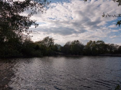 sunset over a lake in spring with moving waves ripples and clouds with trees around water in spring beauty