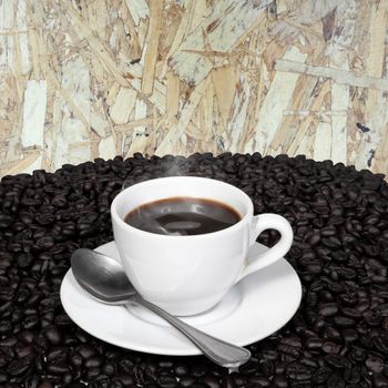 Black coffee in cup and coffee beans with smoke on old wood board background.