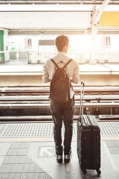 Man is on the train station with travel bag, using mobile phone, wait for a train