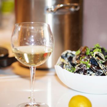 Steamed mussels in cheese sauce. Mussels in shells in the bowl with white wine on the table.